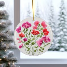 a white ornament with pink and red flowers on it next to a christmas tree