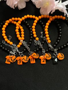 an orange and black beaded necklace with two charms on it, next to flowers