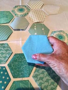 a hand holding a piece of blue and green paper over some hexagonal tiles