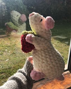 a stuffed animal is sitting on a window sill and holding a flower in it's mouth