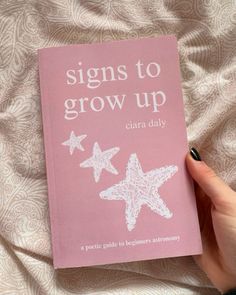 a hand holding a pink book with white stars on it and the title signs to grow up