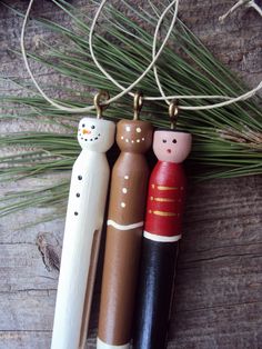 three wooden toy figures hanging from a string on a wood table with pine needles and branches