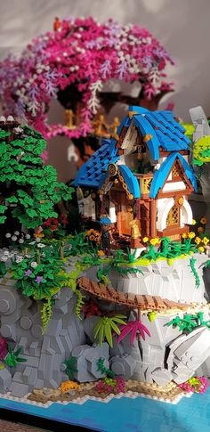 a lego model of a house on top of a hill with trees and flowers around it