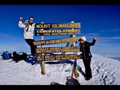 two people standing at the top of a mountain with their arms in the air and holding up signs