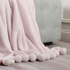 a light pink blanket with pom - poms on the floor next to a couch