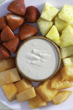 a white plate topped with sliced pineapples and strawberries next to a dip