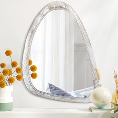 a mirror sitting on top of a table next to a vase filled with yellow flowers