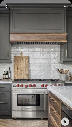 a kitchen with gray cabinets and stainless steel stove top oven, wood counter tops, and white subway backsplash