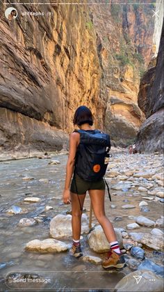 a woman standing on rocks in the middle of a river with a backpack over her shoulder