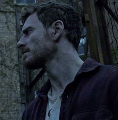 a man standing in front of a building with barbed wire on the fence and looking off into the distance