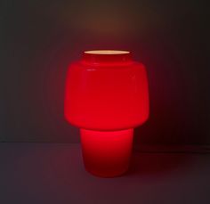 a red vase sitting on top of a table next to a light that is turned on