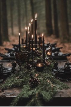 the table is set with candles, plates and pine cones in the middle of the forest