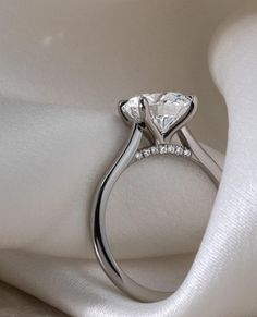 a close up view of a diamond ring on a white cloth with an elegant design