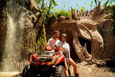 a man and woman are riding an atv in front of a dragon - like structure