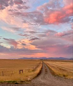 a dirt road in the middle of an open field under a pink sky with clouds