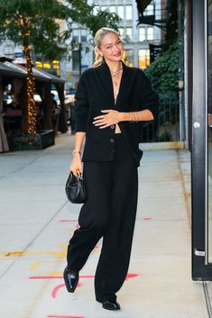 a woman is walking down the sidewalk with her hand on her hip while wearing black