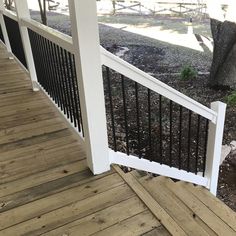 a wooden porch with white railings and black iron hand rails on the side of it