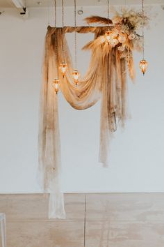 an arrangement of flowers and lights hanging from the ceiling in a room with white walls