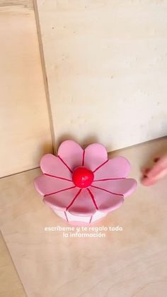 a pink flower shaped vase sitting on top of a wooden table next to a wall