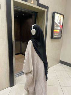 a woman wearing a black and white hijab standing in front of an elevator