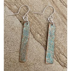 pair of earrings with blue pattered metal bar hanging from earwires on stone surface