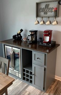 a coffee bar with several cups on the top and two wine glasses hanging above it