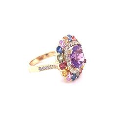 7.13 Carat Cushion Cut Amethyst Sapphire Diamond Yellow Gold Cocktail Ring  Amethyst, Multi-Colored Sapphires and Diamond Cocktail Ring! A beautiful and sparkly combination of colorful beauty!  This one of a kind piece has been carefully designed and curated by our in house designer!  This ring has a vibrant Cushion Cut Amethyst that weighs 3.55 Carats and is embellished with 16 Multi-Colored Sapphires that weigh a total of 3.02 Carats as well as 38 Round Cut Diamonds that weigh 0.56 Carats (Cla Luxury Multicolor Sapphire Ring With Gemstone Accents, Dazzling Oval Multi-stone Gemstones, Oval Multi-stone Gemstones, Multicolor Diamond Gemstones With Accents, Luxury Purple Gemstones With Halo Setting, Luxury Multicolor Amethyst Ring With Gemstone Accents, Multicolor Oval Amethyst Ring, Purple Diamond Ring With Gemstone Accents, Multicolor Sapphire Ring With Diamond Accents