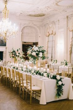 a long table with white flowers and greenery is set up for a formal function