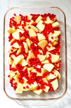 a glass dish filled with sliced apples and pomegranates on top of a white table