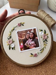 a person holding up a photo in front of a embroidery hoop with flowers on it