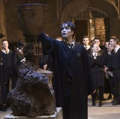 harry potter standing next to a fountain with his hands in the air, surrounded by other people