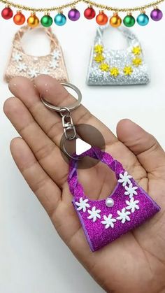 a hand holding a purple purse shaped keychain with white flowers on the front