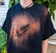 a man standing in front of a house wearing a t - shirt with an image of a leaf on it