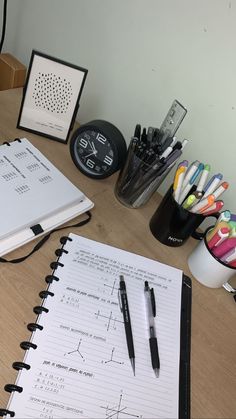 an open notebook sitting on top of a wooden table next to pens and pencils