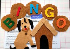 a dog is sitting in front of a house made out of felt and letters that spell i n g o