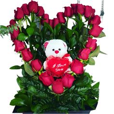 a teddy bear sitting on top of a bouquet of roses with a heart shaped pillow