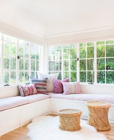 a white room with lots of windows and pillows on the window sill next to two wicker baskets