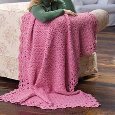 a woman sitting on a couch covered in a pink crochet blanket with her arms crossed