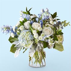 a bouquet of white and blue flowers in a glass vase on a light blue background