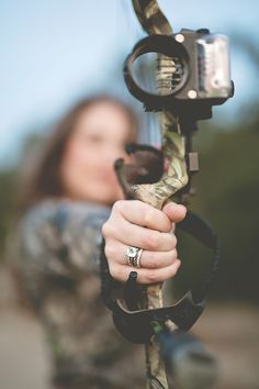 a woman is holding a bow and aiming it with her hand while wearing an engagement ring