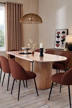 a dining room table with chairs and a vase on the end, in front of a window