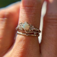 a woman's hand holding a ring with a white opal and diamonds on it