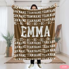 a woman holding up a brown and white personalized blanket with the word team on it