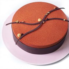 a round cake on a white plate with gold beads and chocolate ribbon around the edge