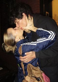 a man and woman kissing each other in front of a brick wall with a handbag on it