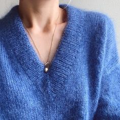 a close up of a person wearing a blue sweater and silver earring necklaces