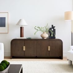 a living room with white couches and green plants on top of a wooden cabinet