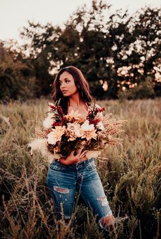 a woman standing in tall grass holding flowers