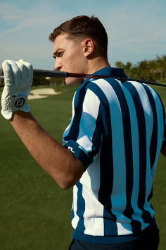 a man holding a baseball bat on top of a lush green field with trees in the background