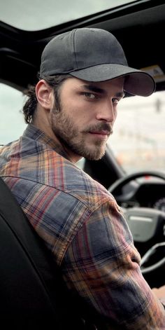 a man sitting in the driver's seat of a car wearing a baseball cap